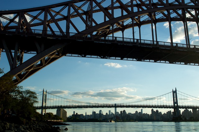 View of sun setting behind a sailboat in the East River behind the Robert F. Kennedy Triborough Bridge and NYC skyline from Astoria Park