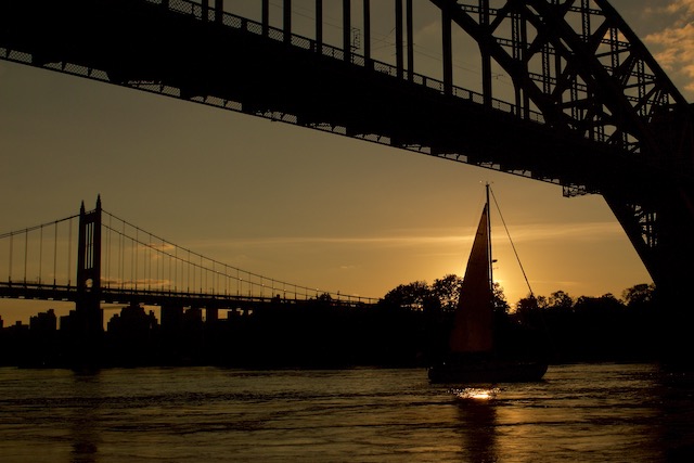 View of sun setting behind a sailboat in the East River behind the Robert F. Kennedy Triborough Bridge from Astoria Park